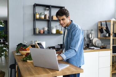Lächelnder Mann mit Laptop in der Küche zu Hause - GIOF14101