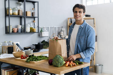 Smiling man with shopping bag and vegetables in kitchen - GIOF14111