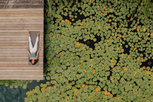 Woman lying on exercise mat while doing yoga at jetty - DAWF02174