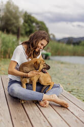 Smiling woman embracing dog at jetty - DAWF02178