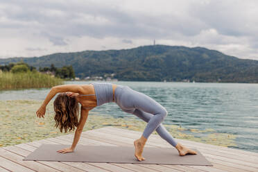 Active woman practicing yoga on jetty by lake - DAWF02180