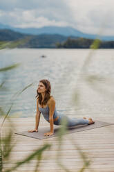 Woman doing push-ups on exercise mat by lake - DAWF02183