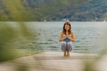 Woman meditating while doing yoga on jetty - DAWF02184