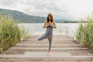 Woman doing tree pose while meditating on jetty - DAWF02188