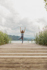 Woman with arms raised doing yoga on jetty - DAWF02189