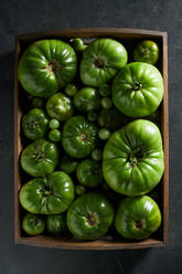 Von oben auf einen schwarzen Tisch gestellte Kiste mit unreifen grünen Tomaten zur Erntezeit - ADSF31653