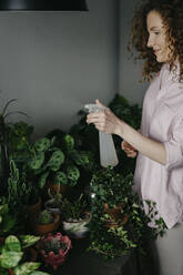 Woman spraying water on plants at home - SEAF00037