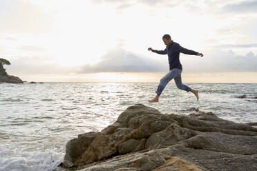 Playful man jumping over rocks near sea at beach - VEGF05186