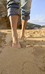 Man with wet legs walking on sand at beach - VEGF05187