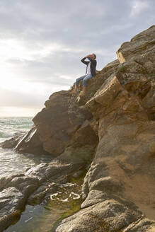 Man sitting on rock shouting at beach - VEGF05191