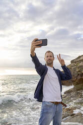 Mann mit Friedenszeichen macht Selfie am Strand - VEGF05198