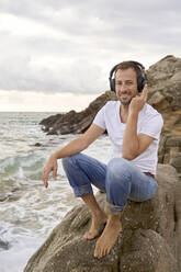 Smiling man listening music on headphones at beach - VEGF05204