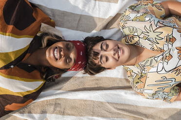 Smiling women lying on picnic blanket at beach - JRVF02049