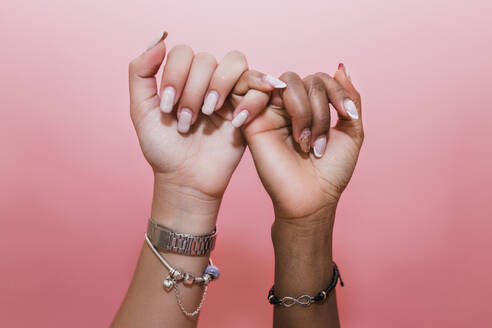 Lesbian couple making pinky promise against pink background - JRVF02079