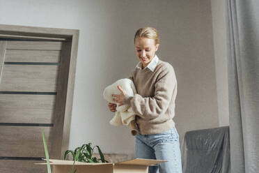 Lächelnde junge Frau beim Auspacken eines Kartons in der neuen Wohnung - VPIF05170