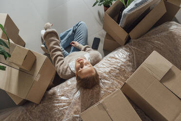 Tired woman resting on plastic wrapped bed at new home - VPIF05190
