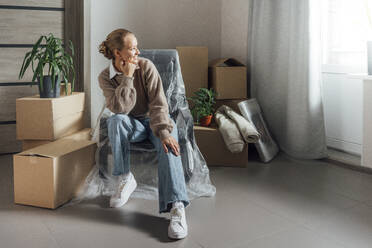 Thoughtful woman with hand on chin sitting at new home - VPIF05206