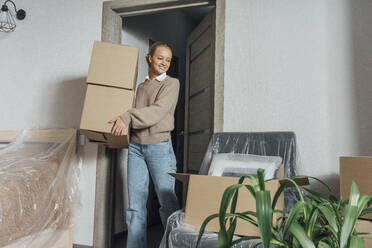 Smiling woman with cardboard boxes relocating in new apartment - VPIF05212