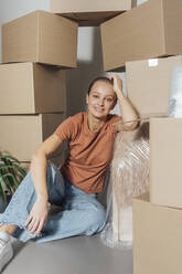 Young woman leaning by cartons at new home - VPIF05228