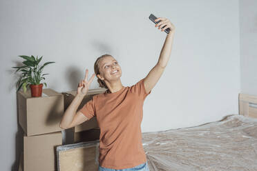 Smiling woman taking selfie with stack of cartons at home - VPIF05233