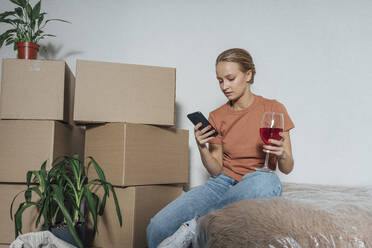 Woman with wineglass using mobile phone in relocated apartment - VPIF05236
