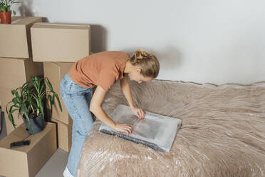 Woman unwrapping picture frame in relocated apartment - VPIF05241