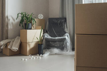 Stack of cardboard boxes with plastic covered armchair in apartment - VPIF05246