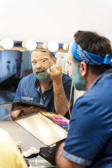 Bearded man applying eyeshadow in dressing room - GPF00153