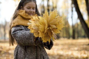 Lächelndes Mädchen schaut auf gelbe Herbstblätter im Park - LLUF00332