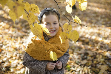 Happy girl looking through branch in autumn park - LLUF00335