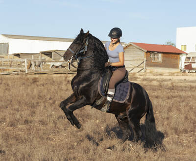 Junge Frau reitet auf einem sich aufbäumenden Pferd auf einer Ranch - FCF02008