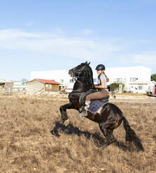 Junge Frau reitet auf einem sich aufbäumenden Pferd auf einer Ranch an einem sonnigen Tag - FCF02009
