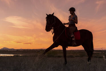 Junge Frau reitet bei Sonnenuntergang auf einem Pferd - FCF02013