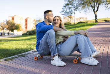 Boyfriend kissing girlfriend on skateboard at park - JCCMF04503