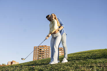 Freund spielt Golf mit Freundin auf einem Hügel - JCCMF04506