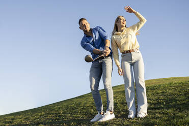 Glückliches Paar spielt Golf auf einem Hügel bei Sonnenuntergang - JCCMF04507