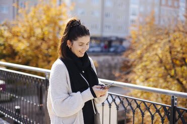 Lächelnde Frau mit Mobiltelefon auf einer Brücke - DAWF02211