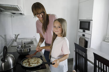 Girl preparing pancake with woman at home - LLUF00339