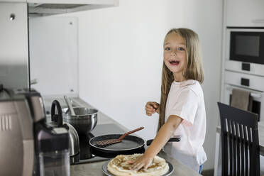 Lächelndes Mädchen mit Pfannkuchen am Küchentisch - LLUF00340