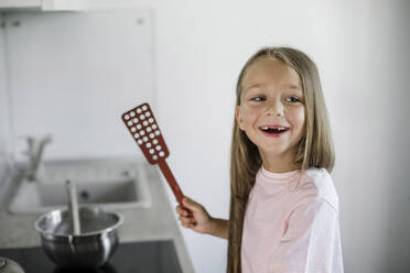 Cute girl holding spatula at home - LLUF00342