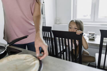 Mädchen sieht Mutter beim Pfannkuchenbacken in der Küche an - LLUF00343