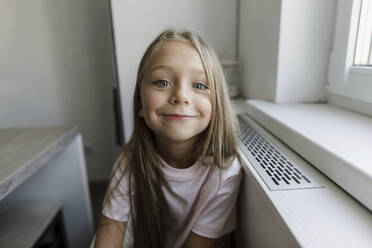 Smiling blond girl sitting at window - LLUF00344