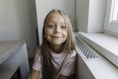 Lächelndes blondes Mädchen sitzt am Fenster - LLUF00344