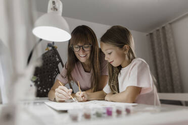 Lächelnde Mutter malt mit Tochter auf Papier zu Hause - LLUF00355