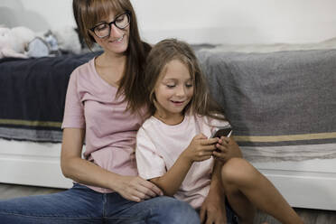 Daughter using smart phone with mother at home - LLUF00358