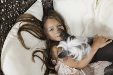 Girl with arm around Chinese Crested dog on chair - LLUF00362