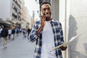 Smiling tourist talking on smart phone in city - PGF00912