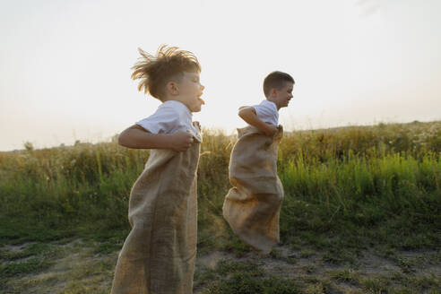 Playful boys jumping with sack at sunset - TYF00034