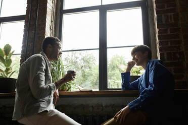 Smiling teenage girl looking at boyfriend having coffee by window - DSHF00084