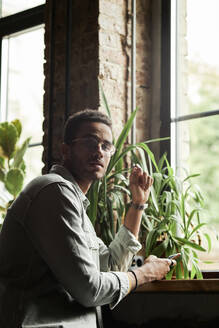 Junger Mann mit Smartphone am Fenster eines Cafés - DSHF00091